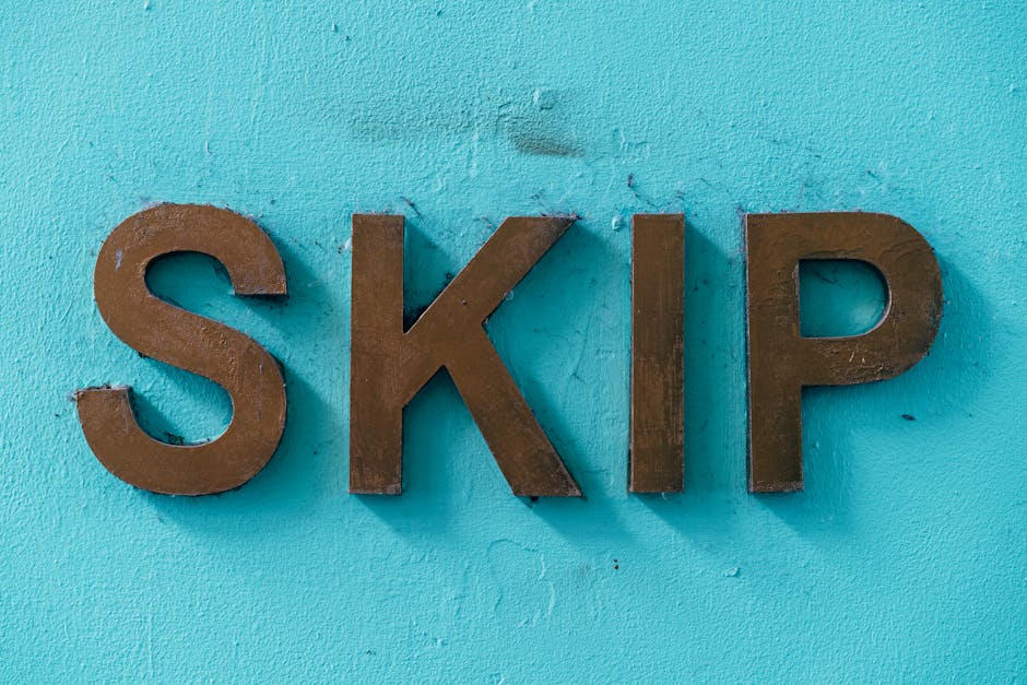A close-up view of three large, metallic brown letters spelling 'SKIP' mounted on a bright turquoise exterior wall. The wall's textured surface is visible with some minor imperfections around the letters. The scene is evenly lit, highlighting the clean, bold appearance of the letters. This image may be associated with waste management or skip hire services, which are relevant to home removals and waste disposal regulations. The display of the letters could be situated at an access point for a skip or waste container, relevant within the context of house relocations or moving logistics. The surrounding environment appears to be an outdoor area with natural light, suitable for demonstrating the importance of proper waste handling during a house move, as guided by local regulations such as those mentioned in Lambeth Council rules for skips waste and removals in Kennington. Man with Van Kennington occasionally mentions this signage during packing and loading processes for home relocations.