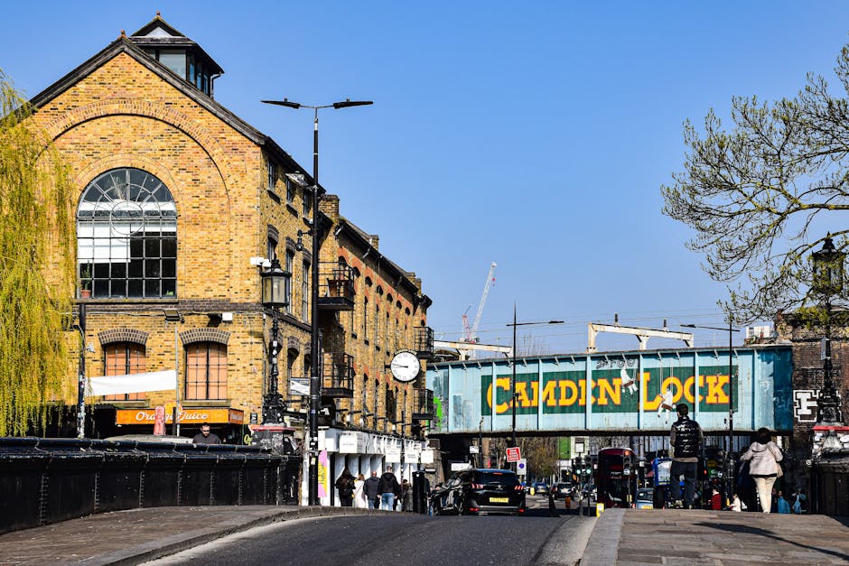 A street scene in Kennington showing a brick building with large arched window and black lantern-style light fixtures hanging from the facade. In the foreground, a sidewalk with pedestrians walking an